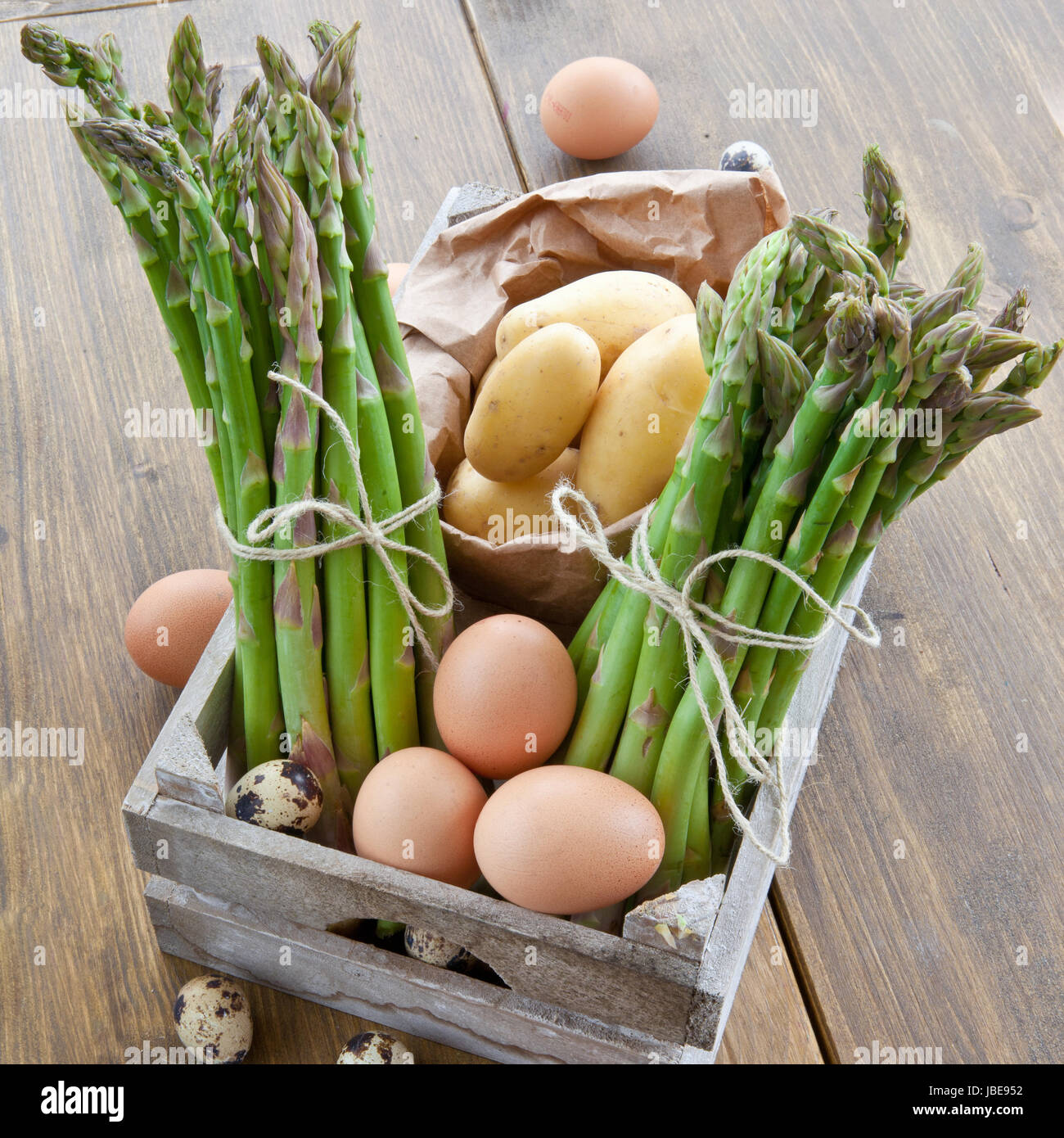 Frischer gruener Spargel , Bio-Kartoffeln und verschiedene rohe Eier in Holzkiste Foto Stock