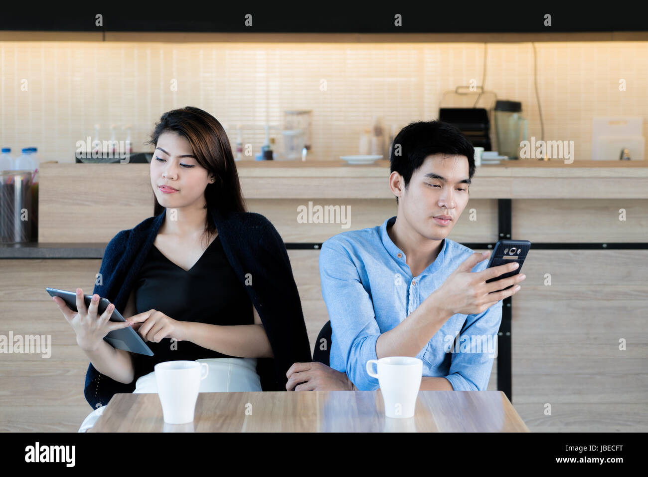 Asian giovane guardando il loro telefono mobile mentre su una data nel cafe. Giovani asiatici giovane seduto e utilizzando il loro smartphone ignorando ogni altro. Foto Stock
