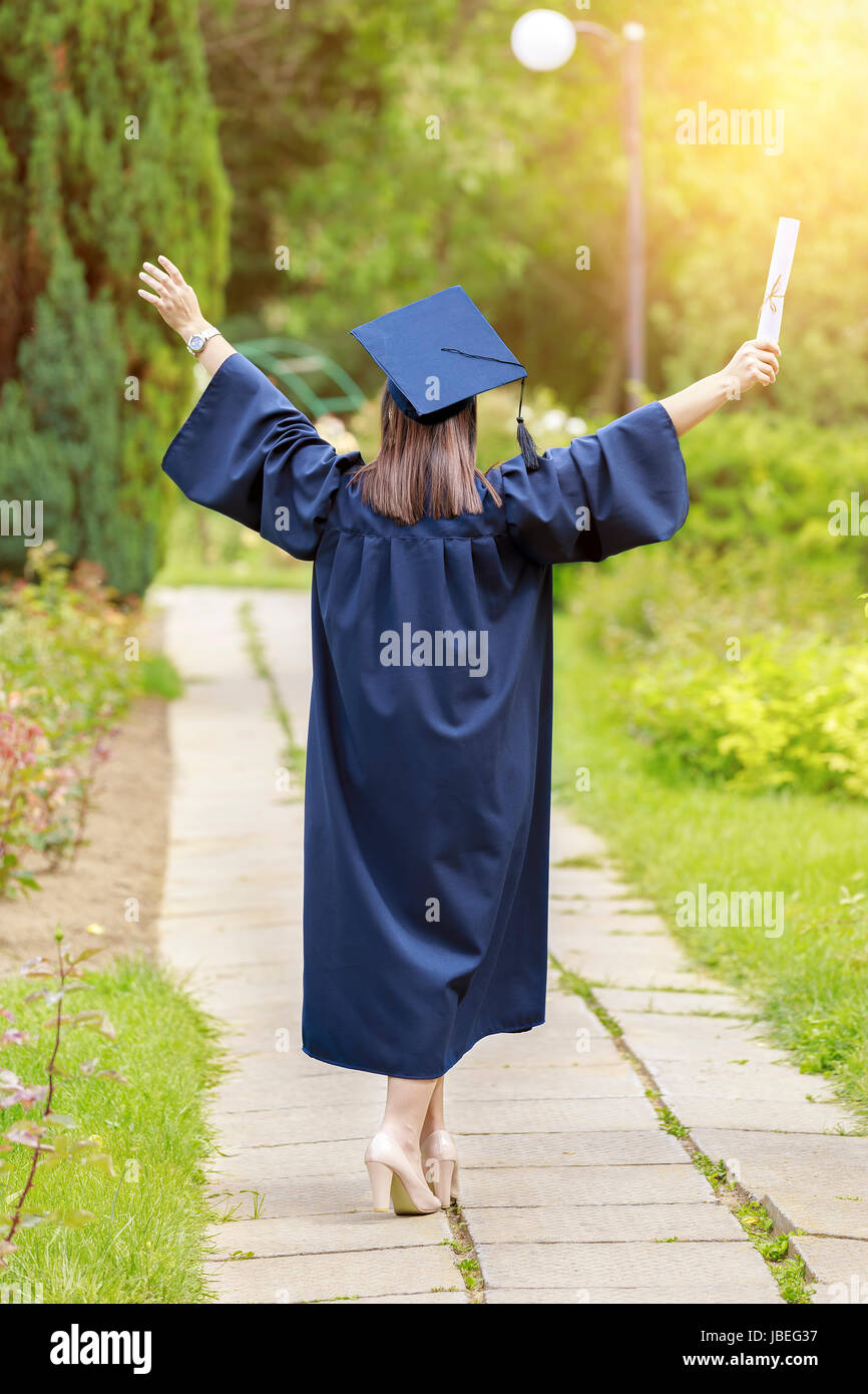 Giovane donna laureata mettere le mani in alto e celebrando con certificato nelle sue mani e nel suo sentimento così la felicità. Foto Stock