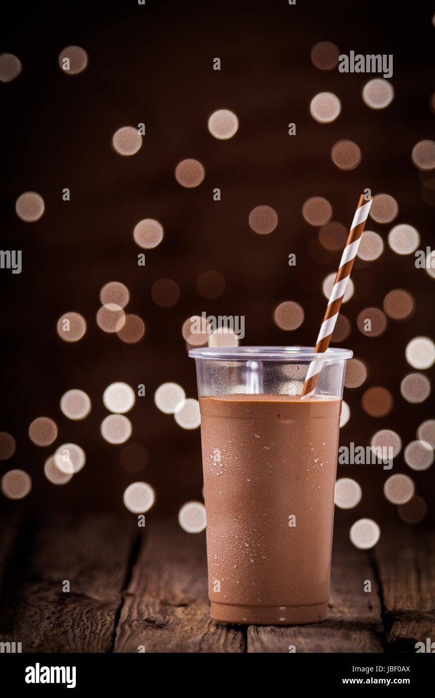 Frullato al cioccolato o frullato con un frizzante bokeh di luci di partito in background in piedi su una tavola in legno rustico in un ristorante o di bar Foto Stock