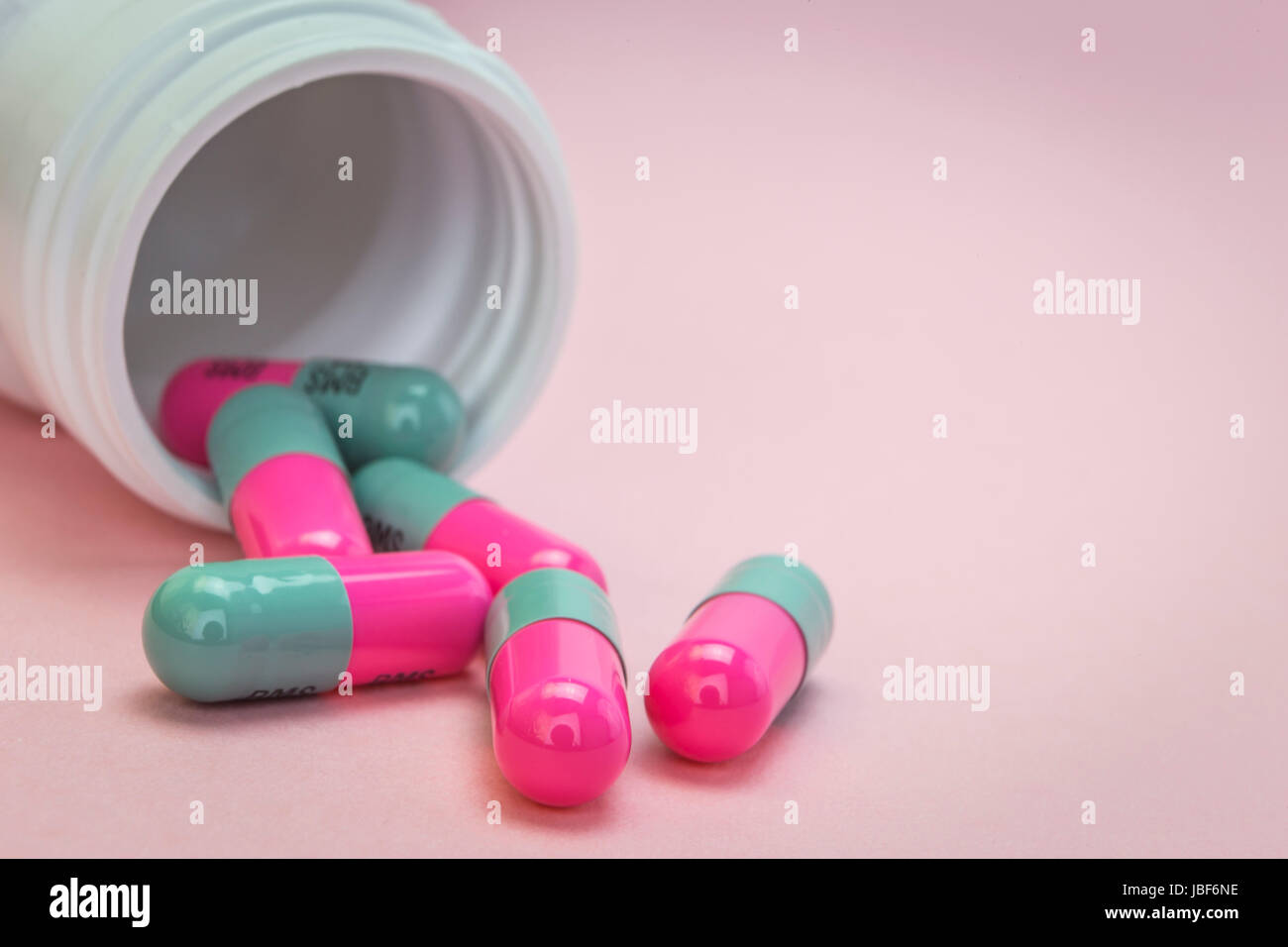 Pills fuoriuscita da una bottiglia aperta isolata su sfondo rosa Foto Stock