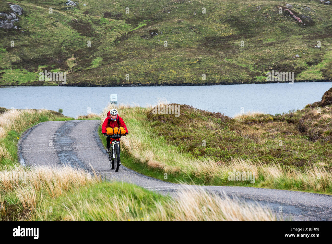 Femmina solitario biker escursioni in bicicletta attraverso le Highlands scozzesi su molto carico touring bicicletta lungo via unica strada in cattive condizioni di tempo piovoso, Scotland, Regno Unito Foto Stock