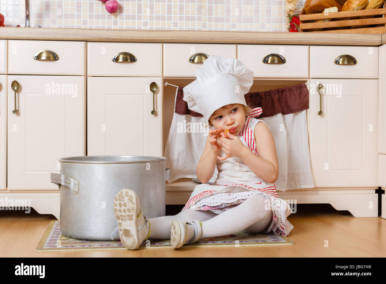 Bambina con grembiule e cappello del cuoco seduta nella cucina di casa.  Madre di helper. 2 anno di età Foto stock - Alamy