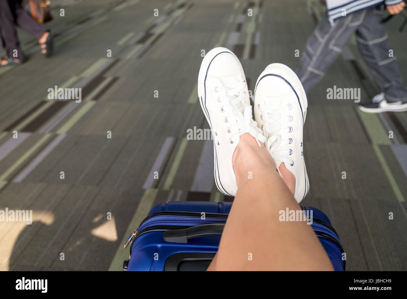 Chiudere fino a croce usura gambe white sneaker giacciono sulla valigia al terminal aeroportuale,Travel Vacation concetto. Foto Stock