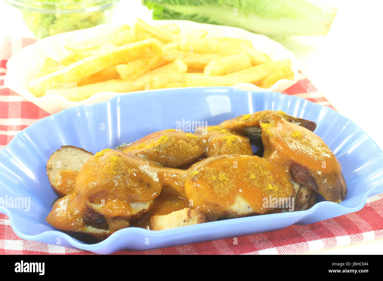 Currywurst mit pommes frites auf einer karierten tovagliolo vor hellem Hintergrund Foto Stock