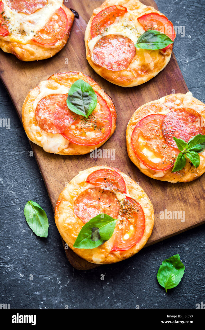 Mini Pizza - freschi fatti in casa mini pizza con salsiccia per pizza, formaggio, pomodori e basilico rustico in pietra nera sfondo con copia spazio. Foto Stock
