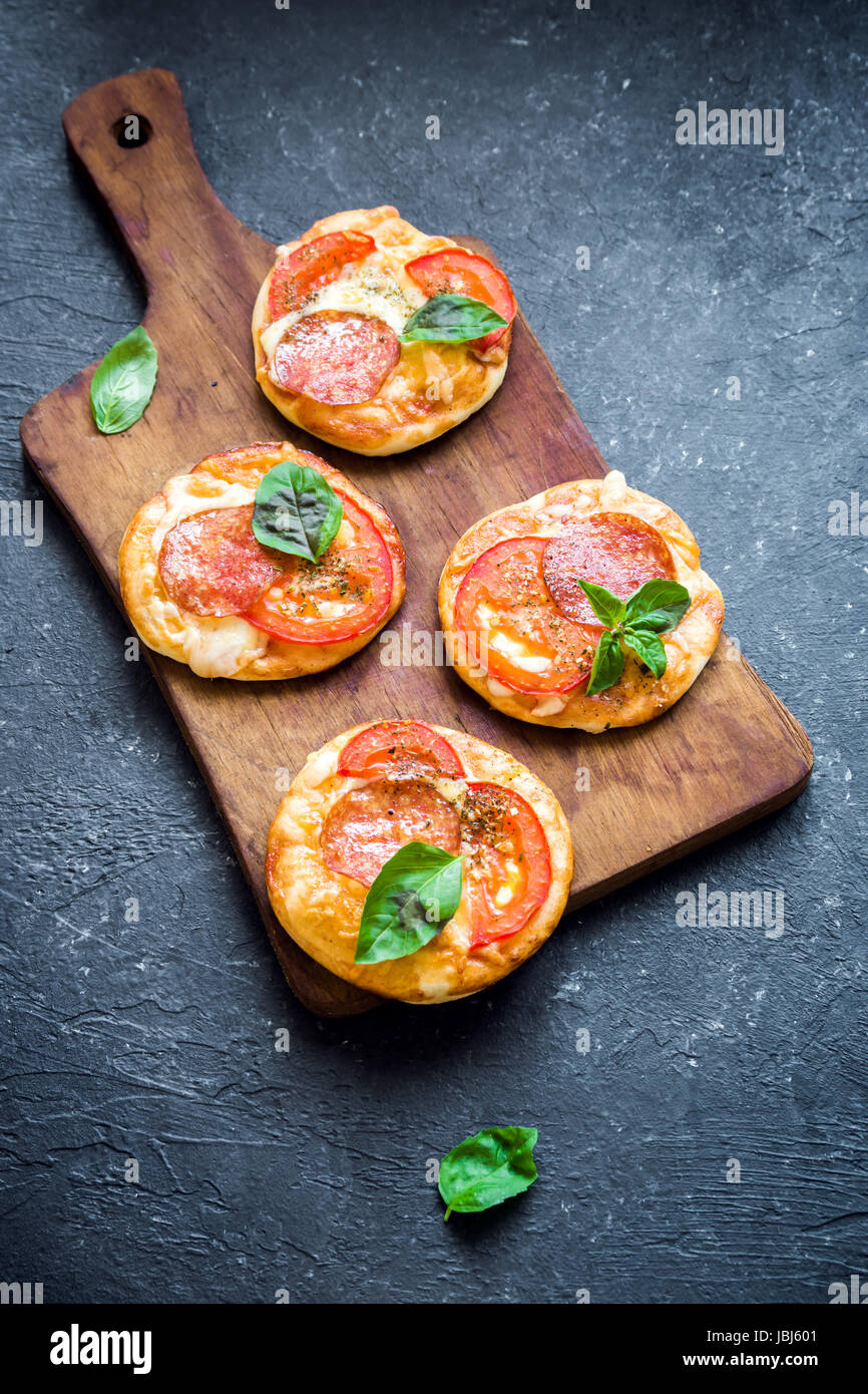 Mini Pizza - freschi fatti in casa mini pizza con salsiccia per pizza, formaggio, pomodori e basilico rustico in pietra nera sfondo con copia spazio. Foto Stock