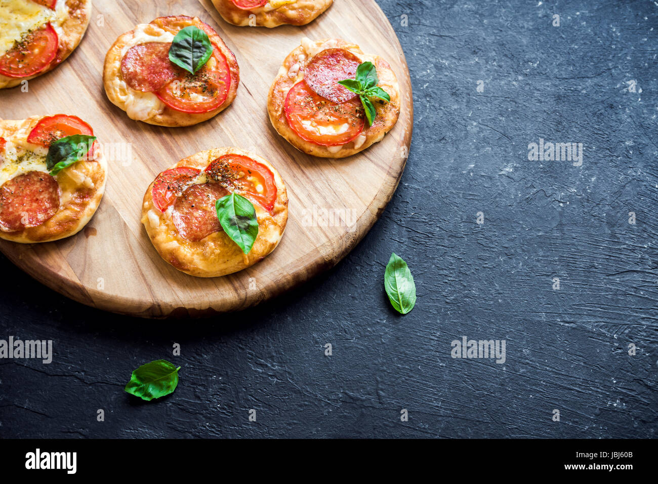 Mini Pizza - freschi fatti in casa mini pizza con salsiccia per pizza, formaggio, pomodori e basilico rustico in pietra nera sfondo con copia spazio. Foto Stock