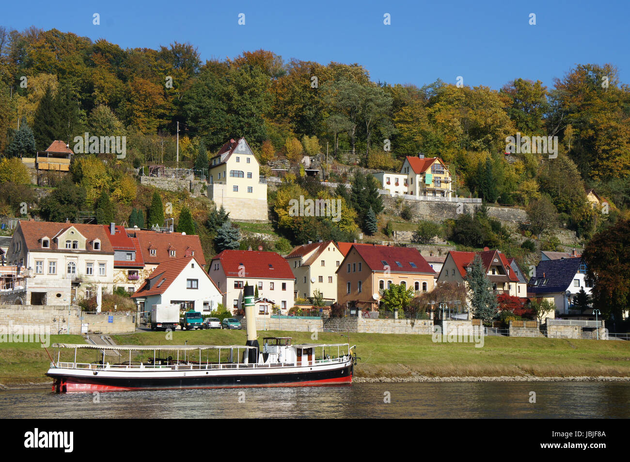 Idyllischer Kurort an der Elbe in der Sächsischen Schweiz in Deutschland, schöne Häuser und bunte Laubwälder, im Vordergrund ein kleiner Dampfer auf der Elbe e idilliaca cittadina termale sull'Elba nella Svizzera sassone in Germania di belle case e coloratissimi boschi di latifoglie, in primo piano di un piccolo sistema di cottura a vapore sul fiume Elba, Foto Stock
