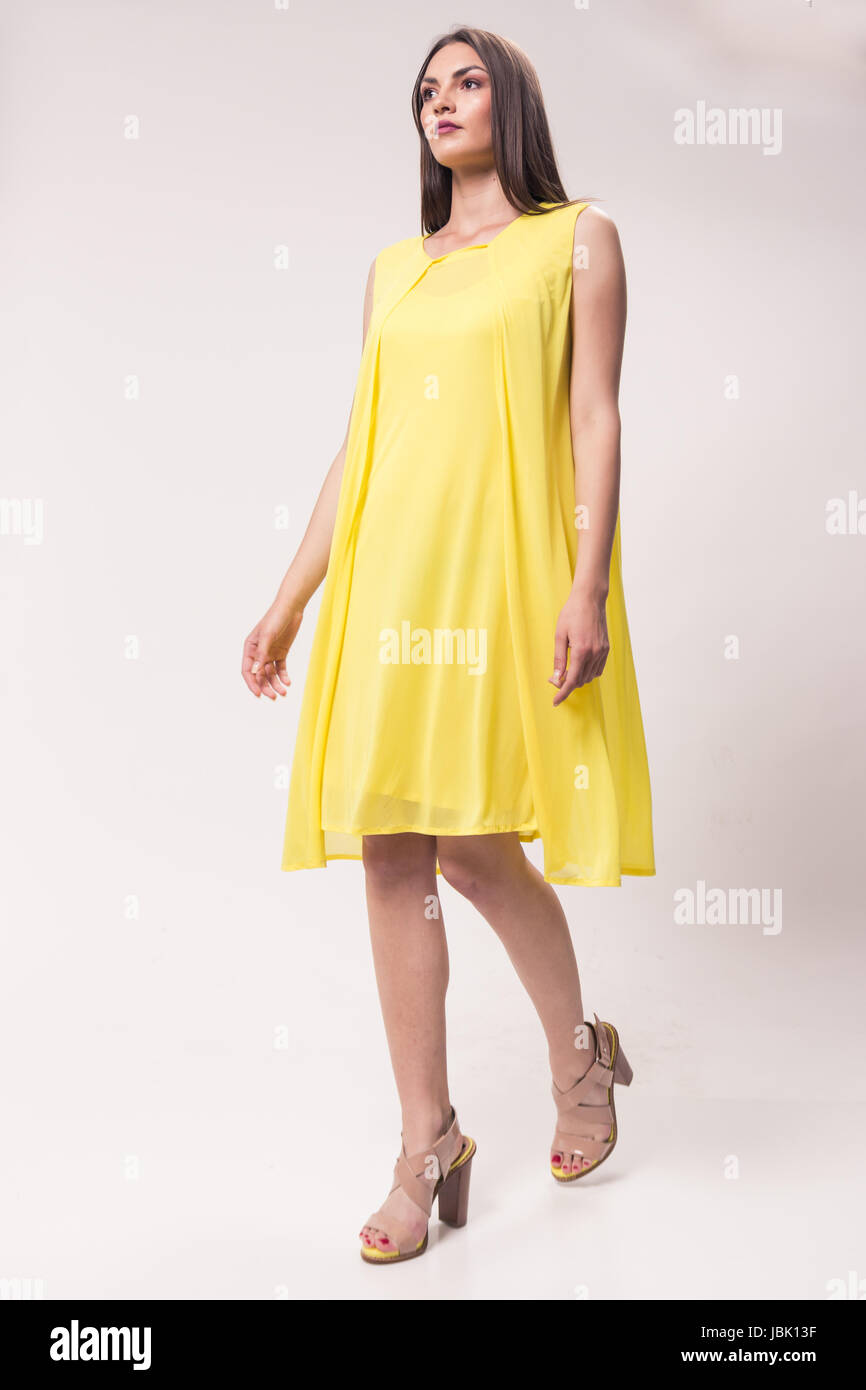 Una giovane donna caucasica, studio, sfondo bianco, giallo abito, tacco alto scarpe alla moda Foto Stock