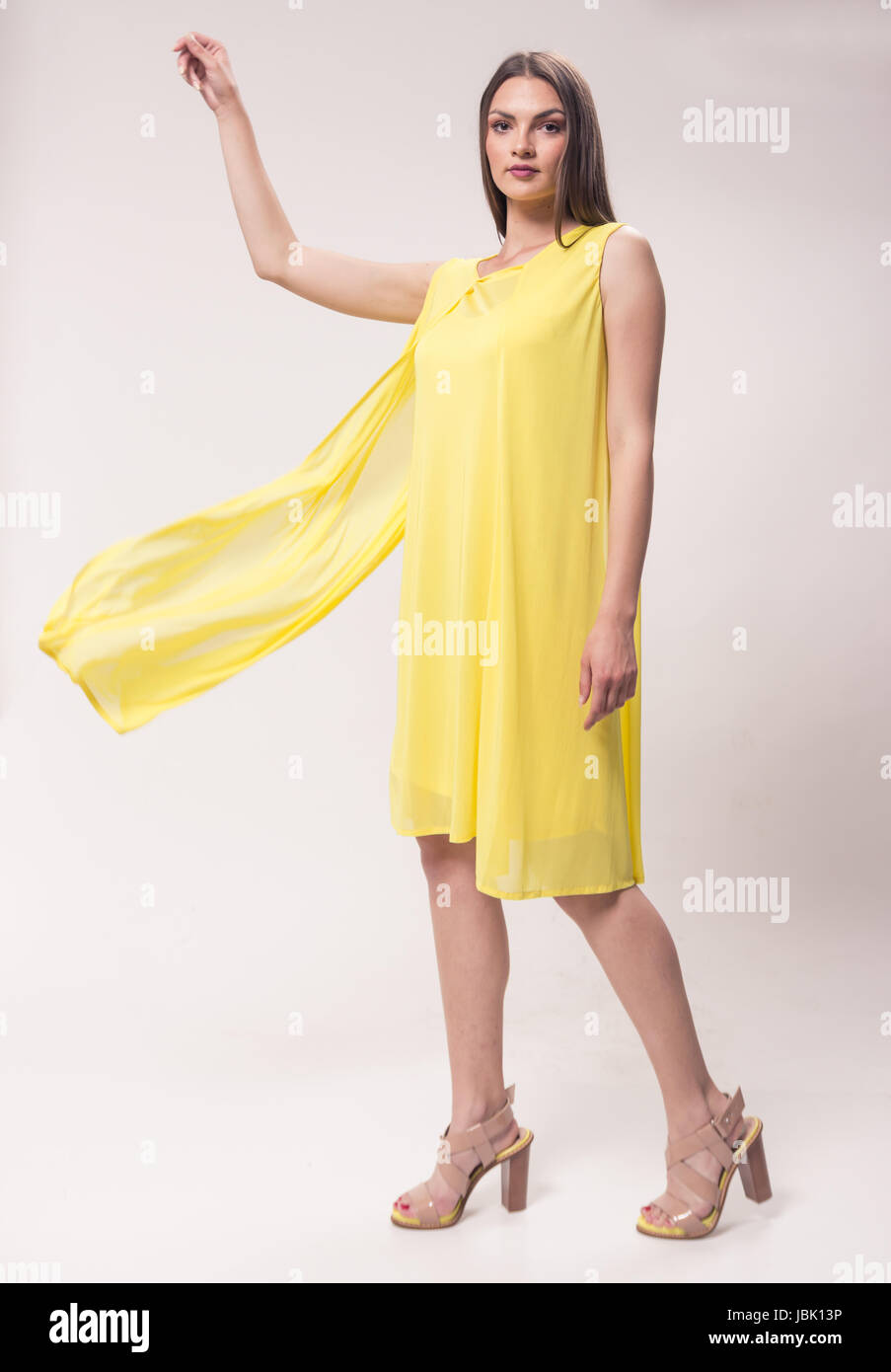 Una giovane donna caucasica, studio, sfondo bianco, giallo abito, tacco alto scarpe alla moda, il movimento di moto Foto Stock