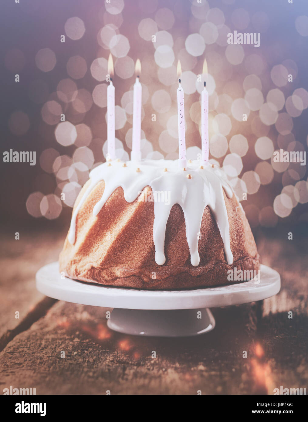 Retrò effetto vintage torta di compleanno con vetrate gocciolamento glassa  bianca decorata con perle e guarnita con quattro parti di masterizzazione  candele con uno sfondo bokeh di luci scintillanti Foto stock 