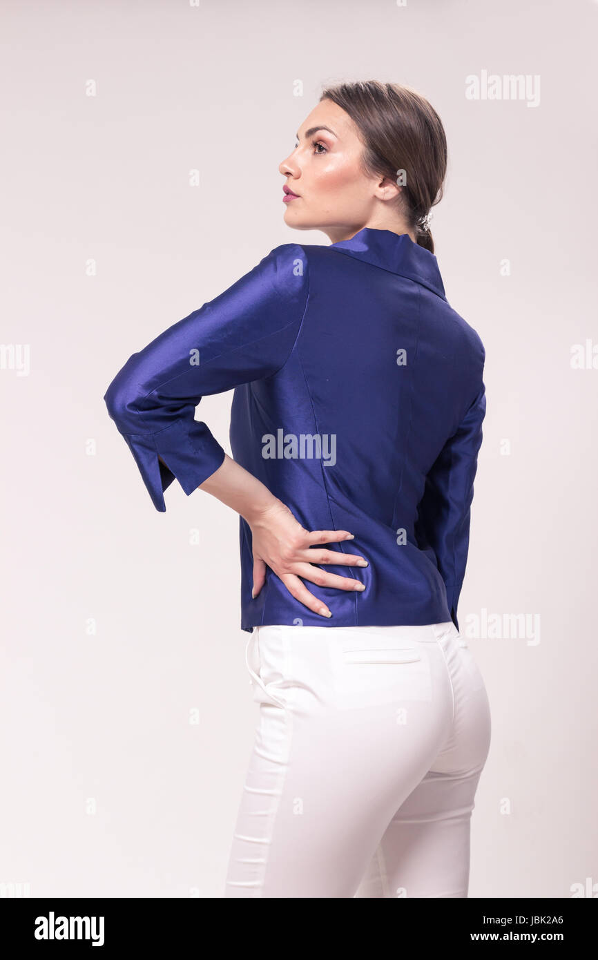Una giovane donna caucasica 20s, 20-29 anni, modello di moda in posa, vista posteriore, retro, studio, sfondo bianco alla moda giacca pantaloni, cercando sideway Foto Stock
