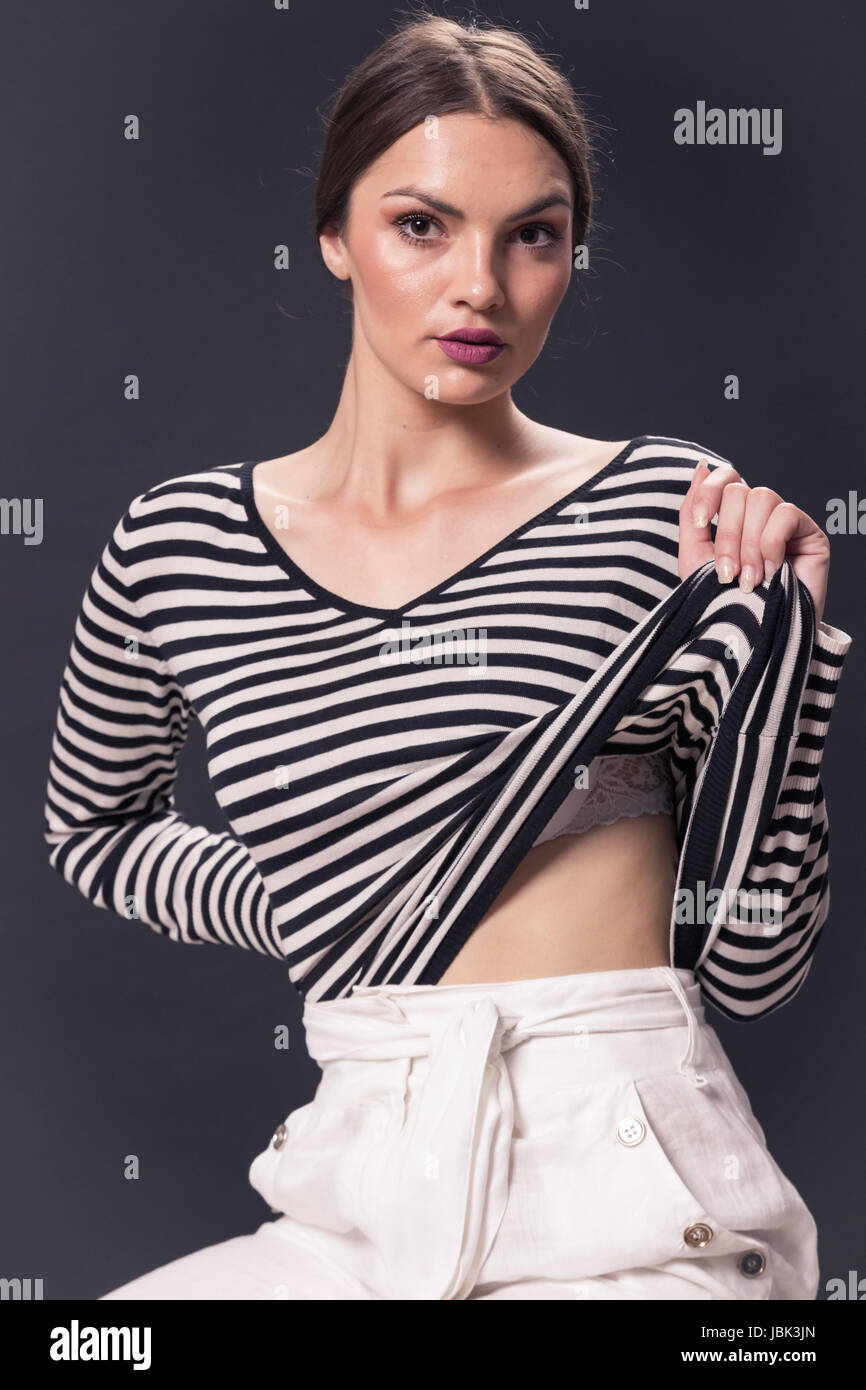 Una giovane donna caucasica 20s, 20-29 anni, moda modello, che pongono, studio, sfondo bianco, striscia orizzontale t-shirt, pantaloni bianchi, guardando alla fotocamera Foto Stock