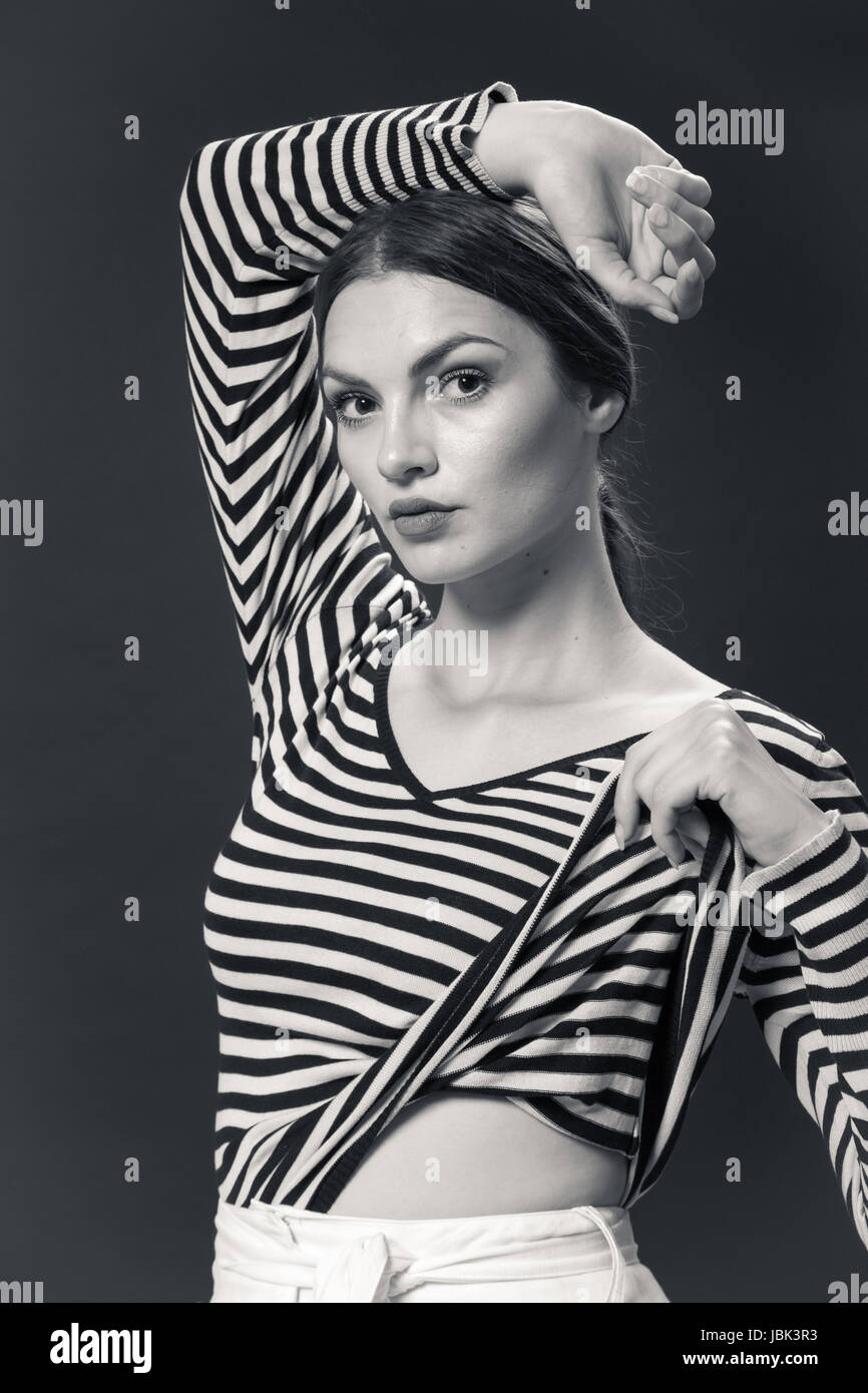 Un giovane caucasico donna sorridente 20s, 20-29 anni, modello di moda, in posa seduta sullo sfondo bianco, studio, striscia orizzontale t-shirt, pantaloni bianchi, alta Foto Stock