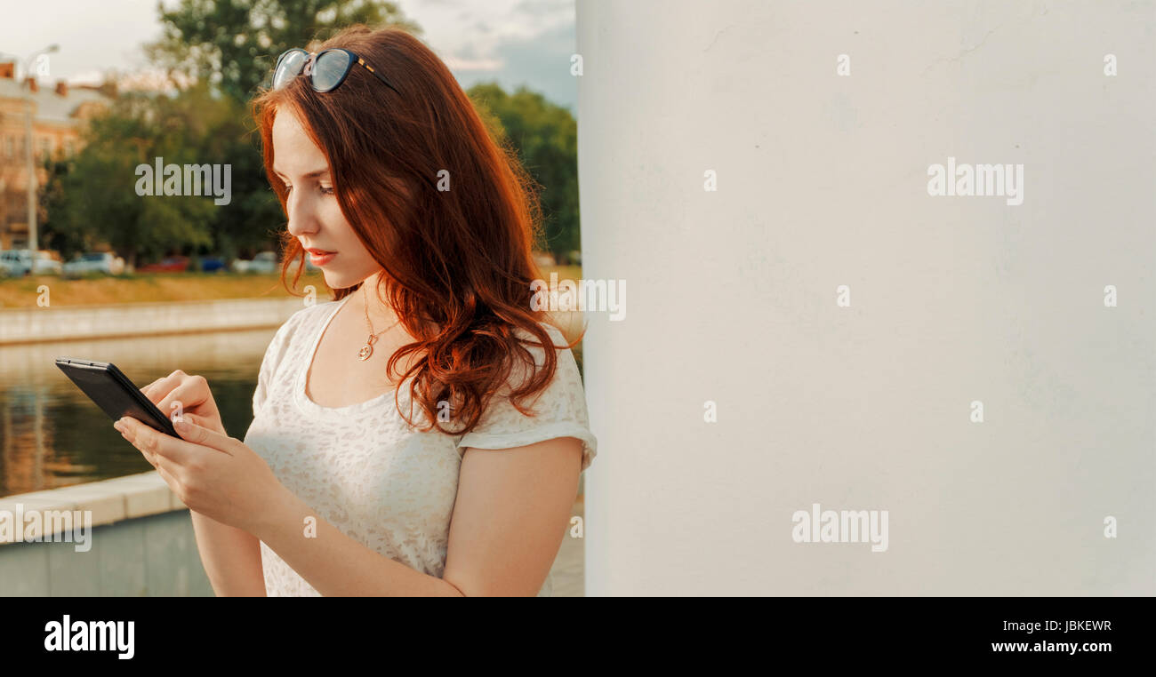 Lo zenzero gravi capelli donna azienda tablet, copyspace sulla parete Foto Stock