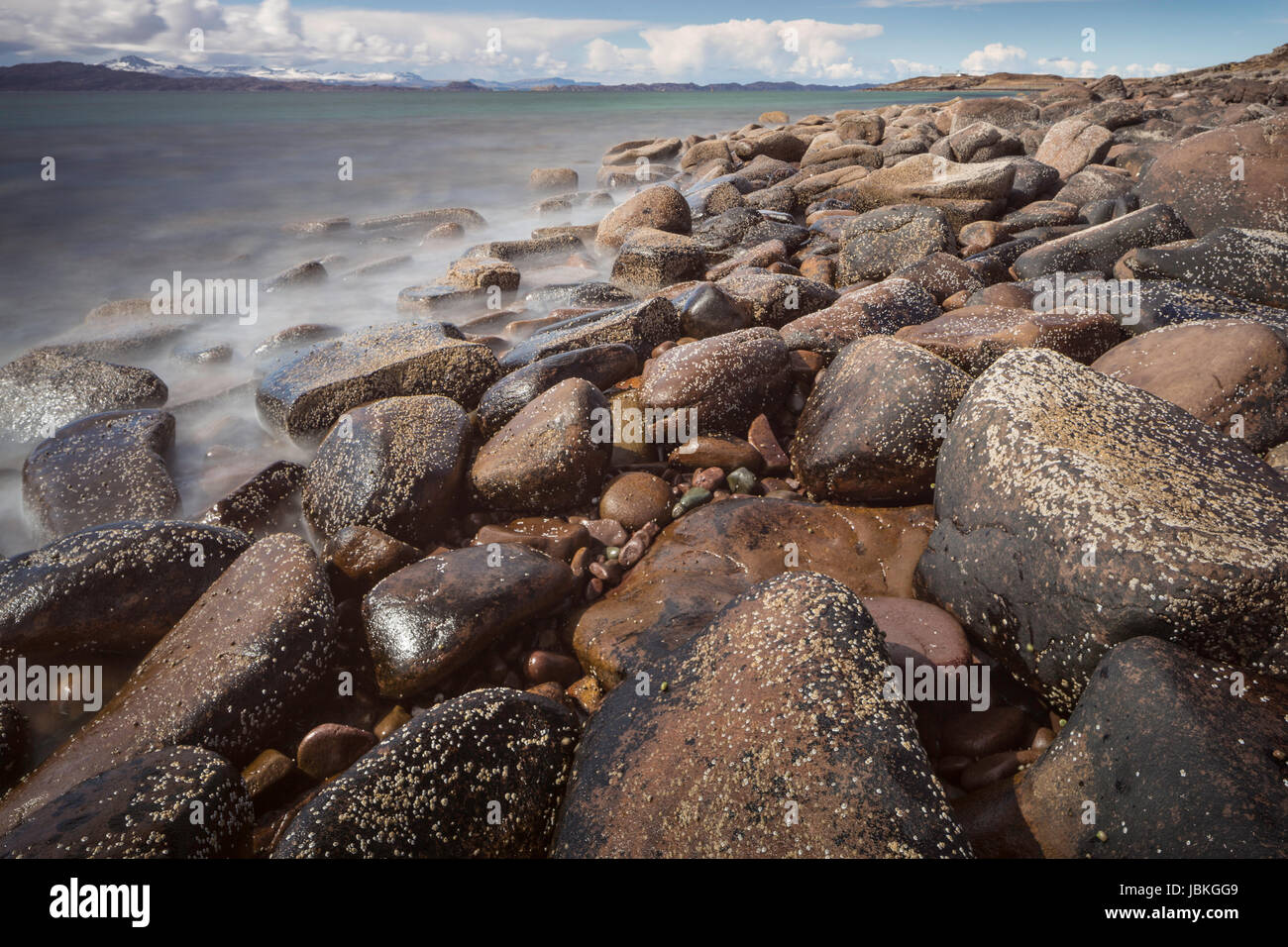 Rocky foreshore vicino Applecross nelle Highlands scozzesi, con il mare e una veduta distante a Rona all'orizzonte; lunga esposizione con Misty Waves Foto Stock