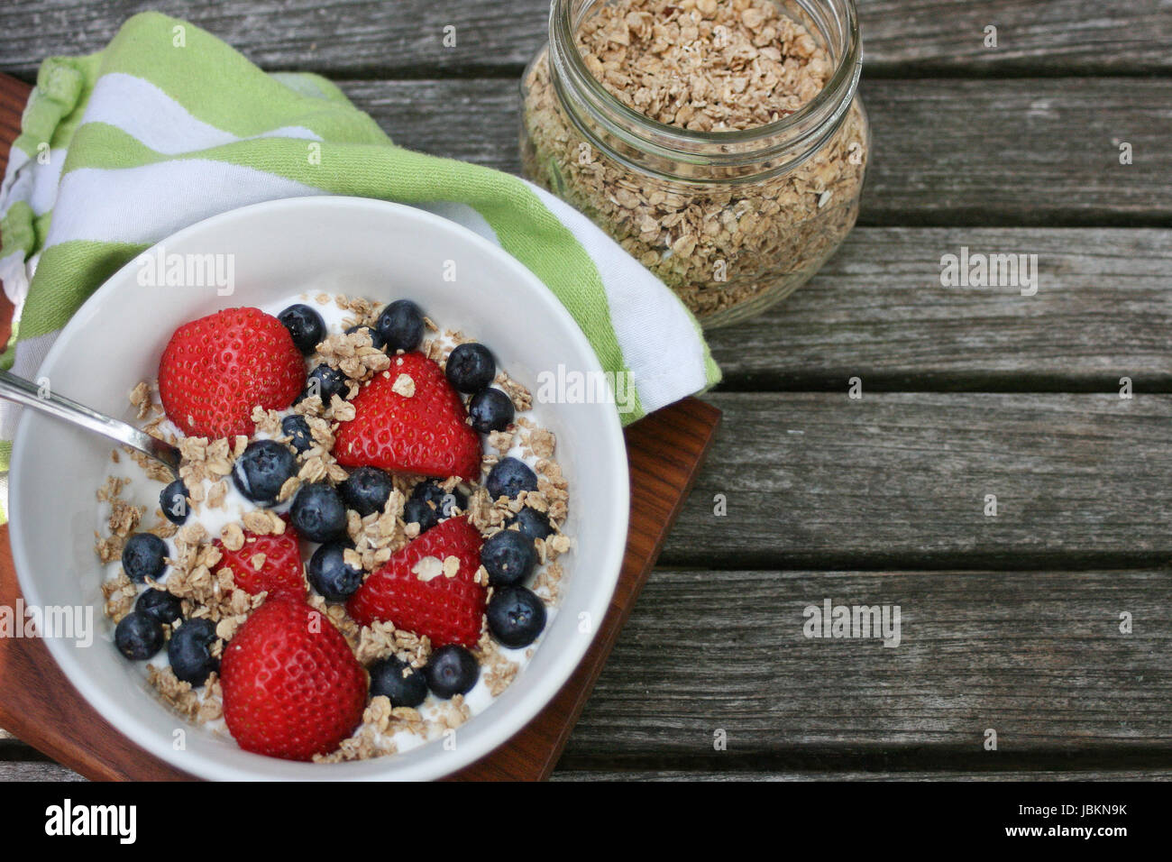 Sana colazione ciotola. Granola in bianco ciotola con lo yogurt greco e bacche su sfondo di legno Foto Stock