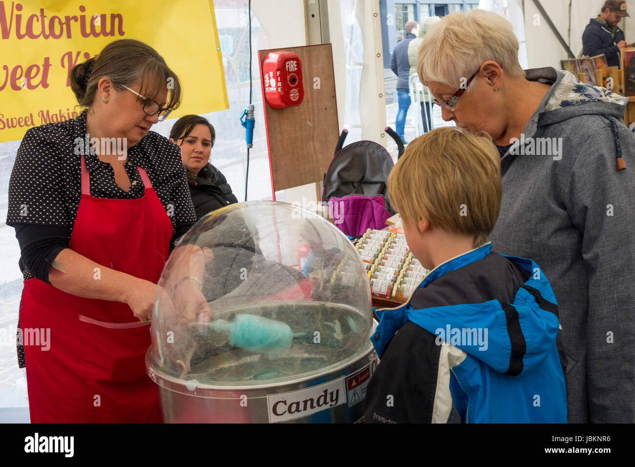 Donna fare Candy Floss su un mercato in stallo mentre una donna e ragazzo il cliente guarda su Foto Stock