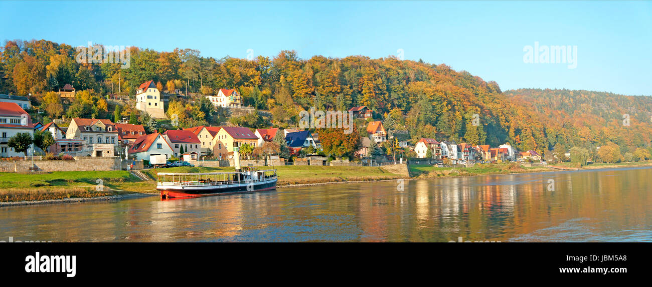 Idyllischer Kurort an der Elbe in der Sächsischen Schweiz in Deutschland, schöne Häuser und bunte Laubwälder, im Vordergrund ein kleiner Dampfer auf der Elbe, panorama idilliaco cittadina termale sull'Elba nella Svizzera sassone in Germania di belle case e coloratissimi boschi di latifoglie, in primo piano di un piccolo sistema di cottura a vapore sul fiume Elba, panorama, Foto Stock