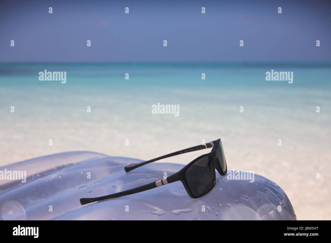 Occhiali da sole su zattera gonfiabile in tropicale oceano blu Foto Stock