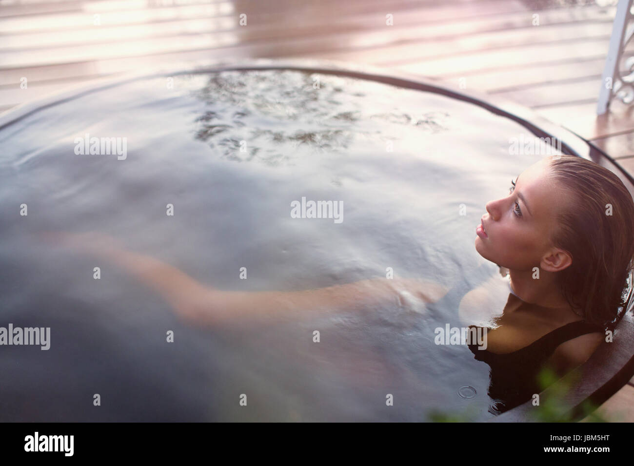 Serena ragazza adolescente in ammollo nella vasca calda sul patio Foto Stock