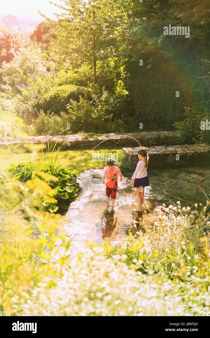 Un ragazzo e una ragazza del fratello e sorella giocando con il tubo flessibile nel soleggiato giardino estivo Foto Stock