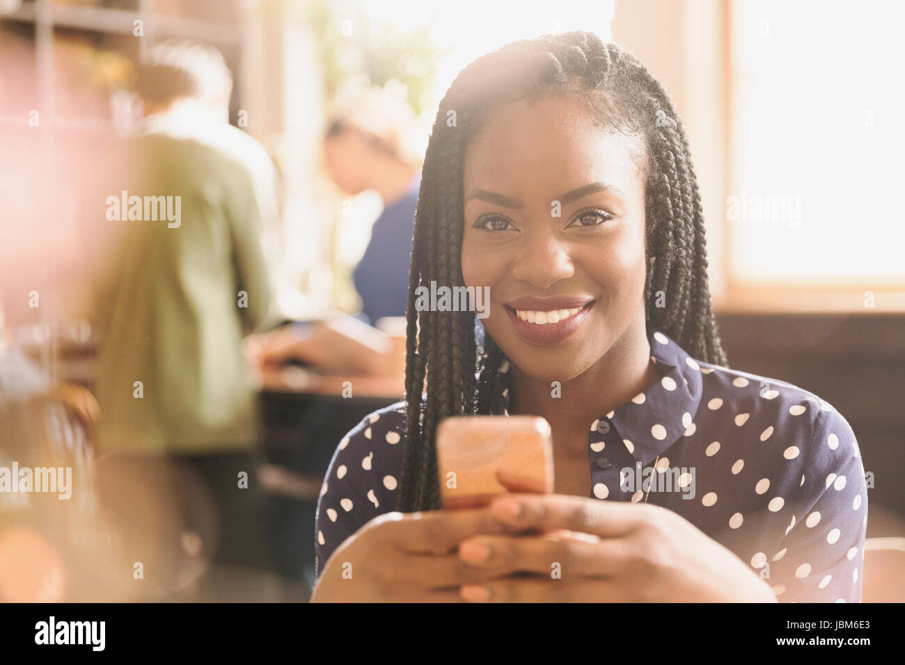 Ritratto sorridente donna africana texting con un telefono cellulare in cafe Foto Stock