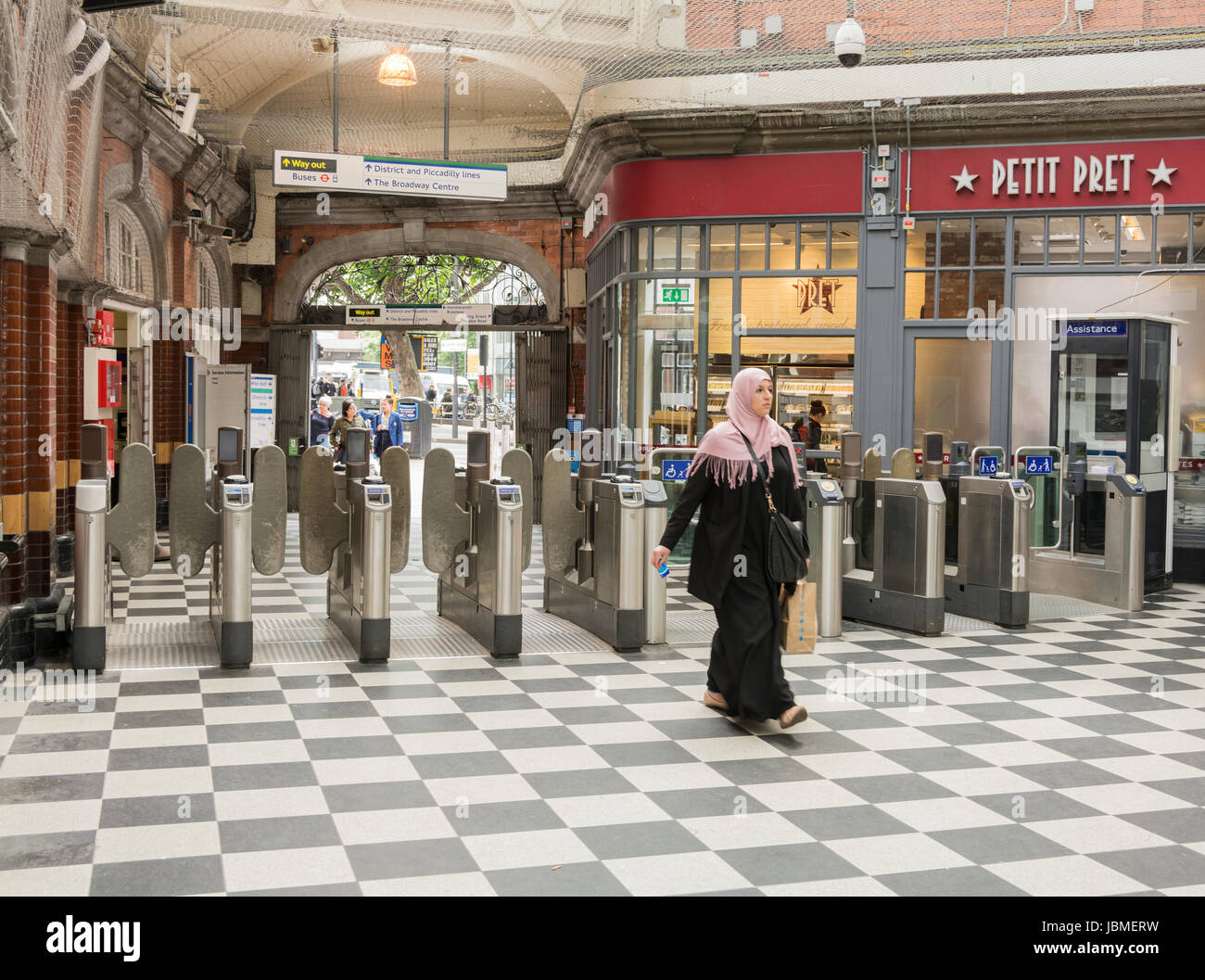 Una donna musulmana in un Hijab passa attraverso le barriere del biglietto a Hammersmith, Cerchio e City Line la stazione della metropolitana di Londra, Regno Unito Foto Stock