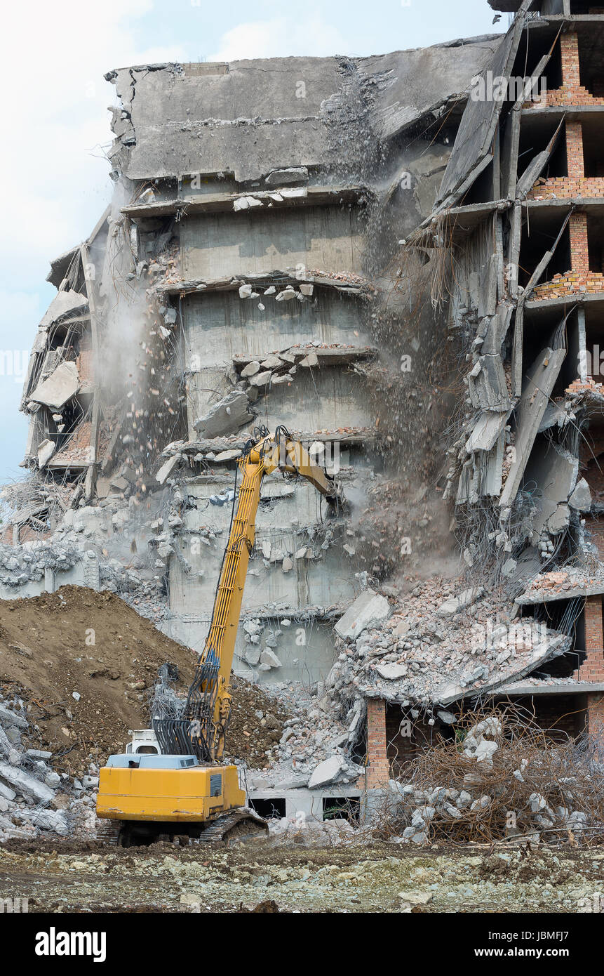 Rimuovere il pericoloso edificio in una zona urbana con un escavatore Foto Stock