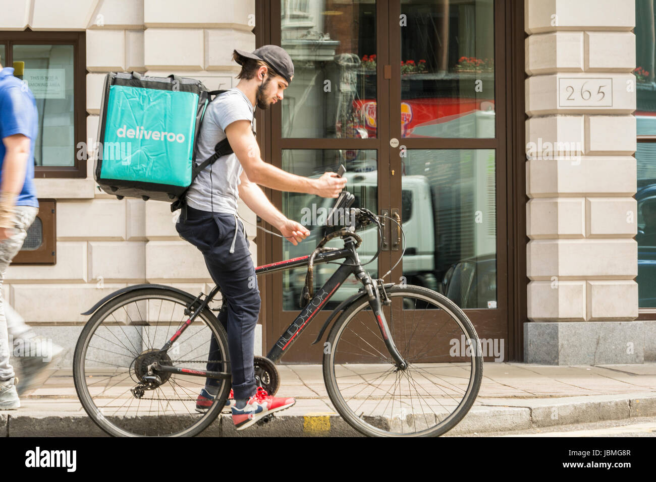 Un ciclista Deliveroo di prelevare il suo lavoro successivo sul suo telefono cellulare nella zona centrale di Londra, Regno Unito Foto Stock