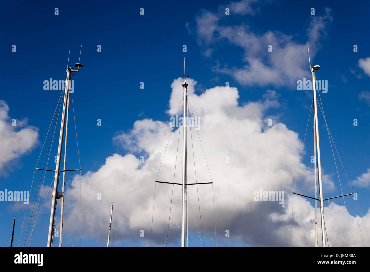 Alcuni alberi di barche a vela su un cielo blu con nuvole di sfondo. Foto Stock