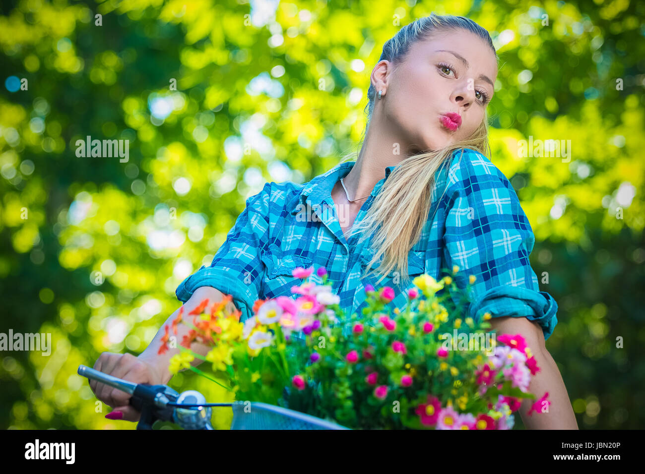 Ritratto di piuttosto giovane femmina con pursed lips alla bicicletta con cesto pieno di fiori colorati. Estate, la natura, la moda e i concetti di ricreazione. Foto Stock