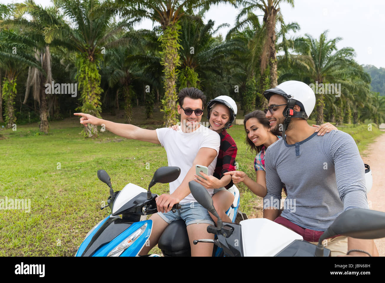 Due giovane in sella moto, giovane uomo e donna utilizzando una cella Smart Phone viaggiare in bicicletta sulla foresta tropicale Road Foto Stock