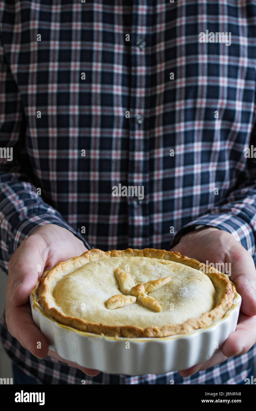 Una metà del tiro di un uomo o di una figura maschile in possesso di una casa fatta di frutta o torta di mele nelle sue mani in un cibo che offre l'immagine. Foto Stock