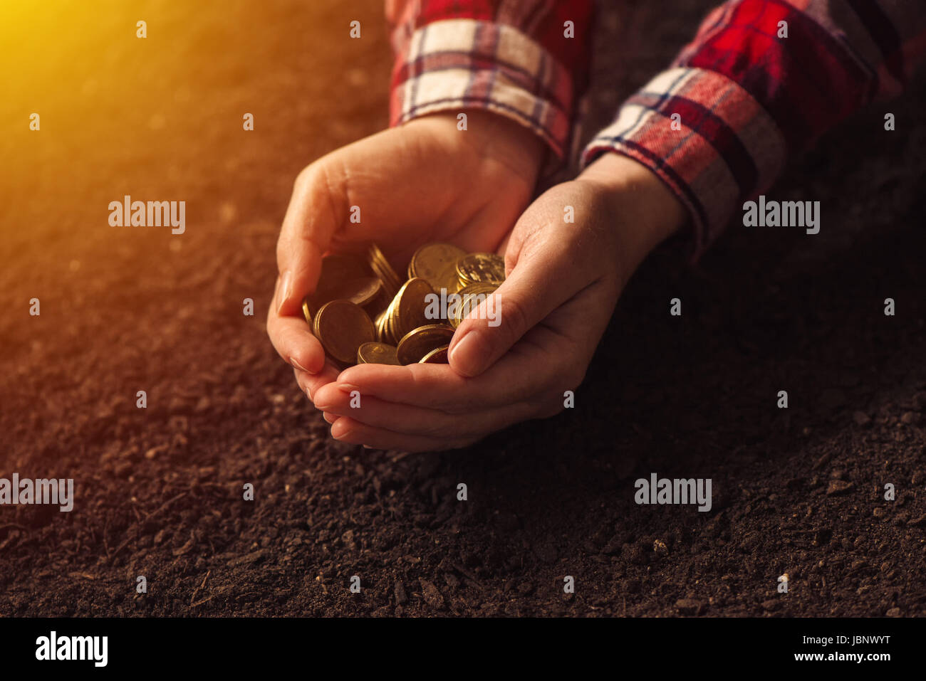 Contadino con manciata di monete al di sopra del suolo, terra di fare soldi e guadagnando il profitto in agricoltura Foto Stock