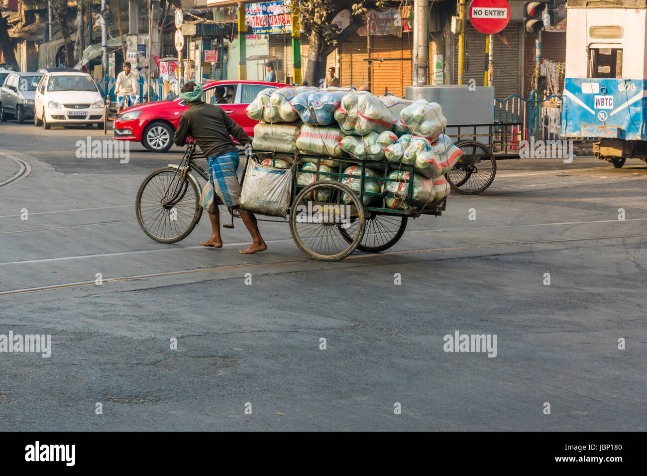 Un pesantemente caricato rikshaw ciclo è attraversare una strada nel sobborgo Esplanade Foto Stock
