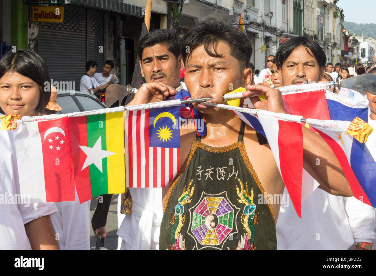 Uomo con le guance trafitto da spiedini con le bandiere dei paesi Asean in un corteo durante i nove imperatore dèi Festival (festival vegetariano) in Phuket Foto Stock