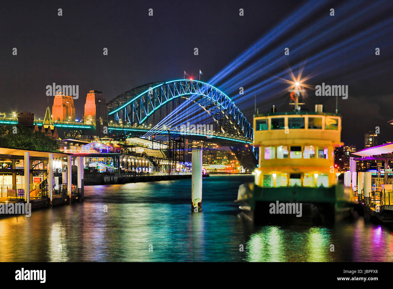 Il Circular Quay ferries pontili verso oltremare terminal passeggeri nelle rocce di Sydney e il Sydney Harbour Bridge di notte durante il Vivid sydney light show. Foto Stock