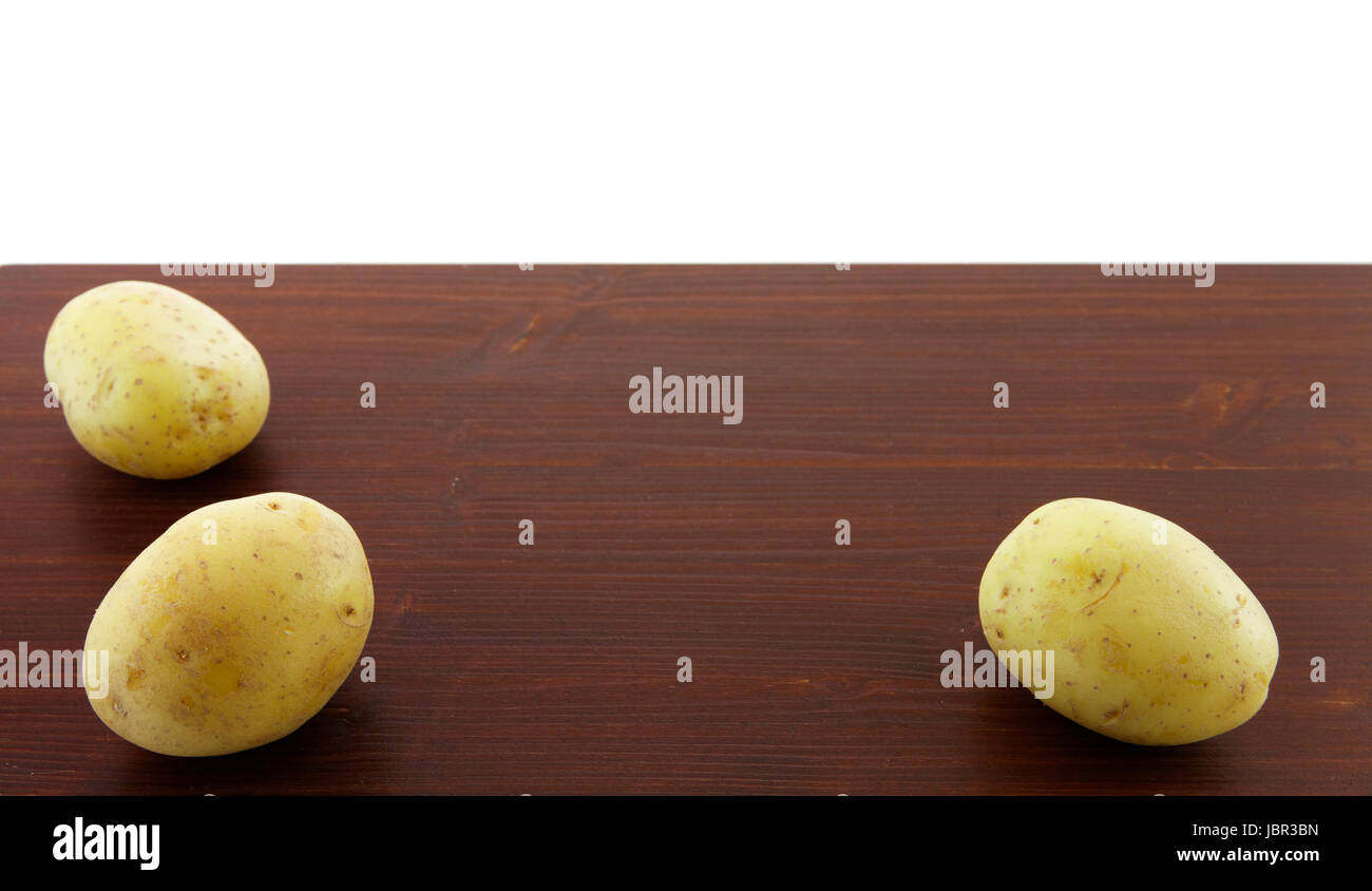 Drei Kartoffelknollen auf einem Holzbrett, mit weißem Hintergrund. Foto Stock