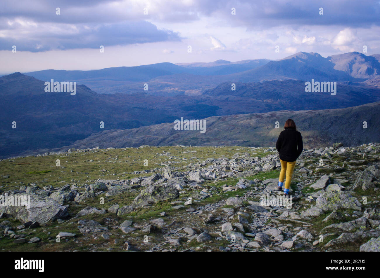 Donna passeggiate lungo la Dow Crag, Inghilterra. Lake District montagne possono essere visti sullo sfondo. Il Tramonto è caduta sulle montagne. Foto Stock