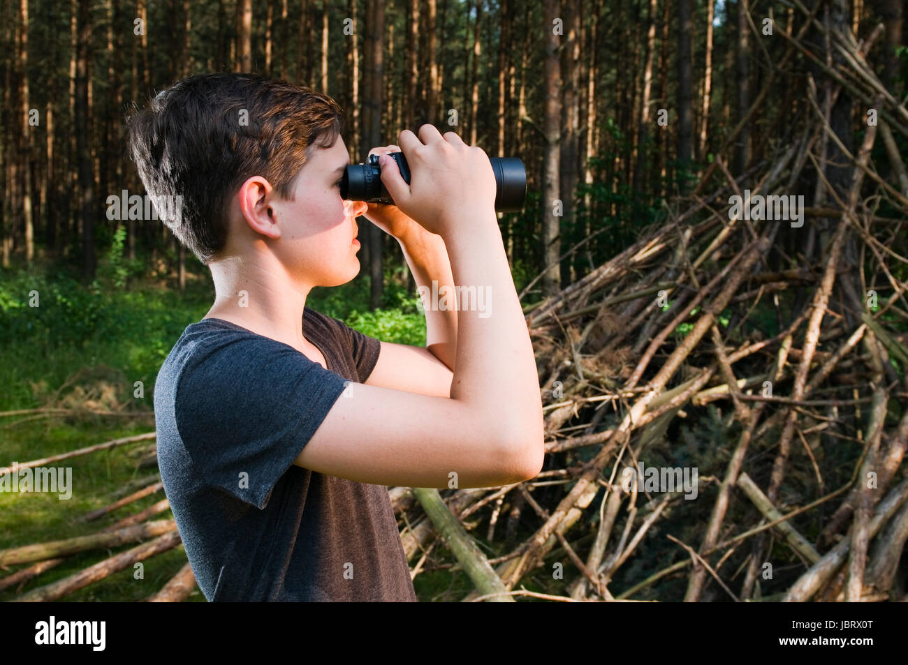 Seitliche Kopf-und-Schulter-Ansicht eines 13jährigen männlichen adolescenti im Wald durch ein Fernglas schauend Foto Stock