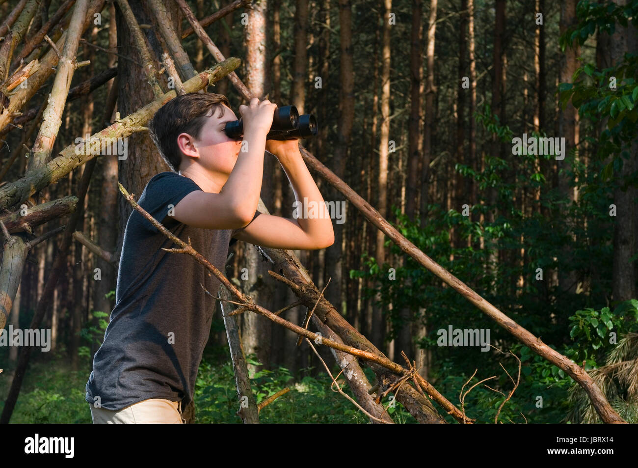 Seitliche Oberkörper-Ansicht eines 13jährigen männlichen adolescenti im Wald durch ein Fernglas schauend Foto Stock