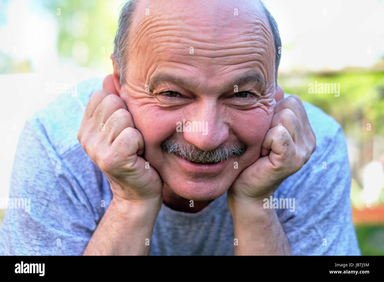 Ritratto di bella anziano uomo con i baffi. Si trova sull'erba sorridente e guardando la telecamera. Foto Stock