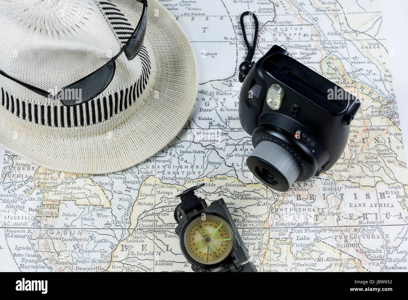 Macchina fotografica d'epoca, occhiali da sole, bussola, cappello bianco su un'antica mappa, che illustra l'emozione e la pianificazione necessari per esplorare una nuova destinazione Foto Stock