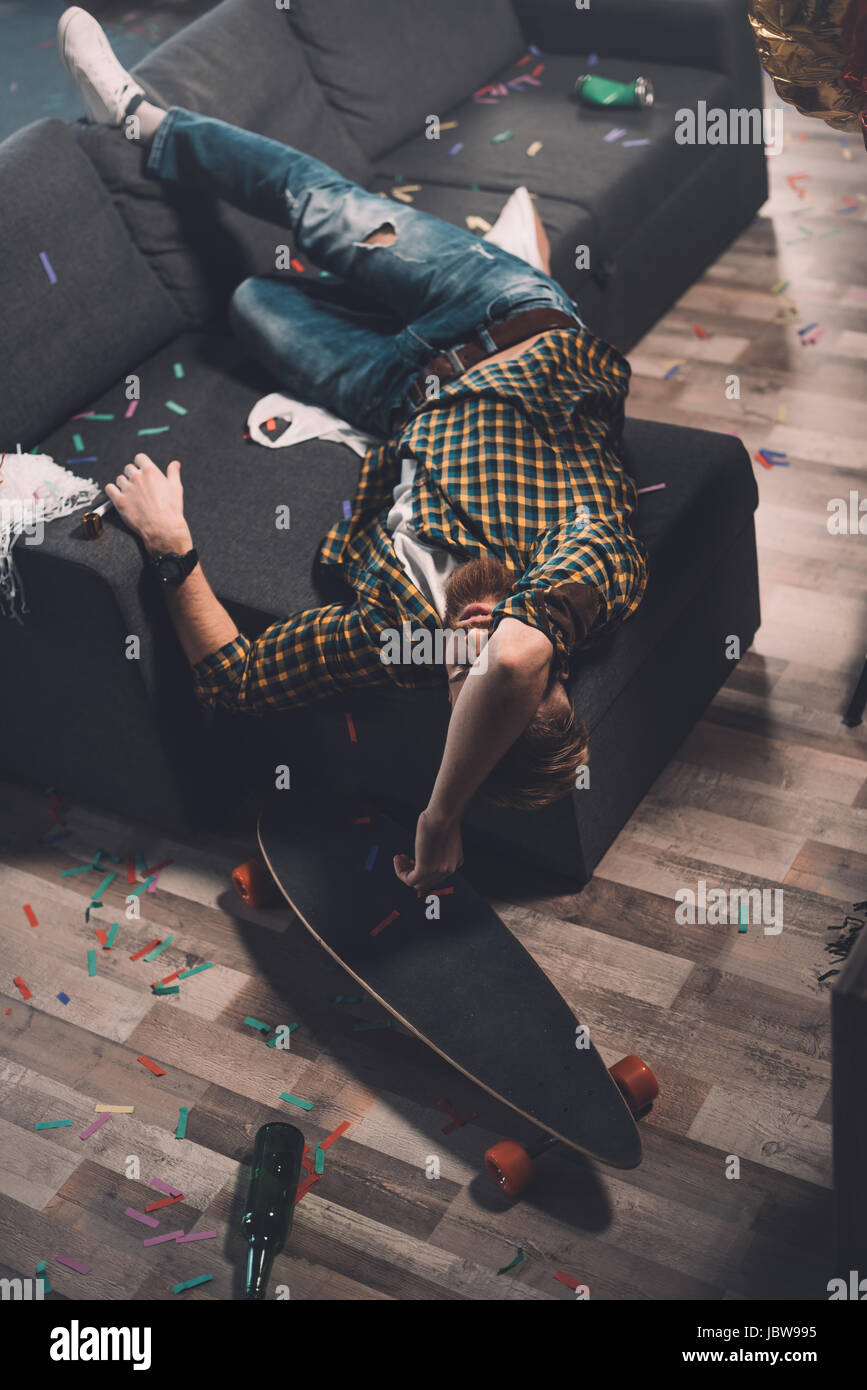 Ubriaco barbuto giovane uomo che dorme sul divano in camera disordinato after party Foto Stock