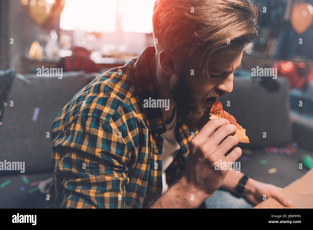 Vista ravvicinata del barbuto giovane con i postumi della sbornia di mangiare la pizza dopo essere partito Foto Stock