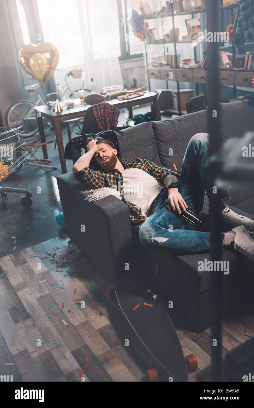 Ubriaco barbuto giovane uomo con bottiglia di dormire sul divano dopo essere partito Foto Stock