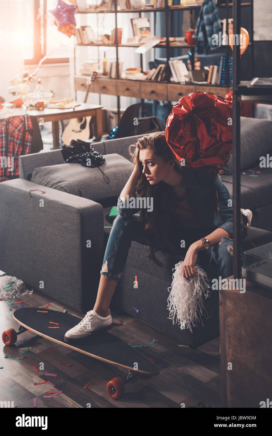 Giovane donna arrabbiato con i postumi della sbornia seduti sul lettino in camera disordinato after party Foto Stock