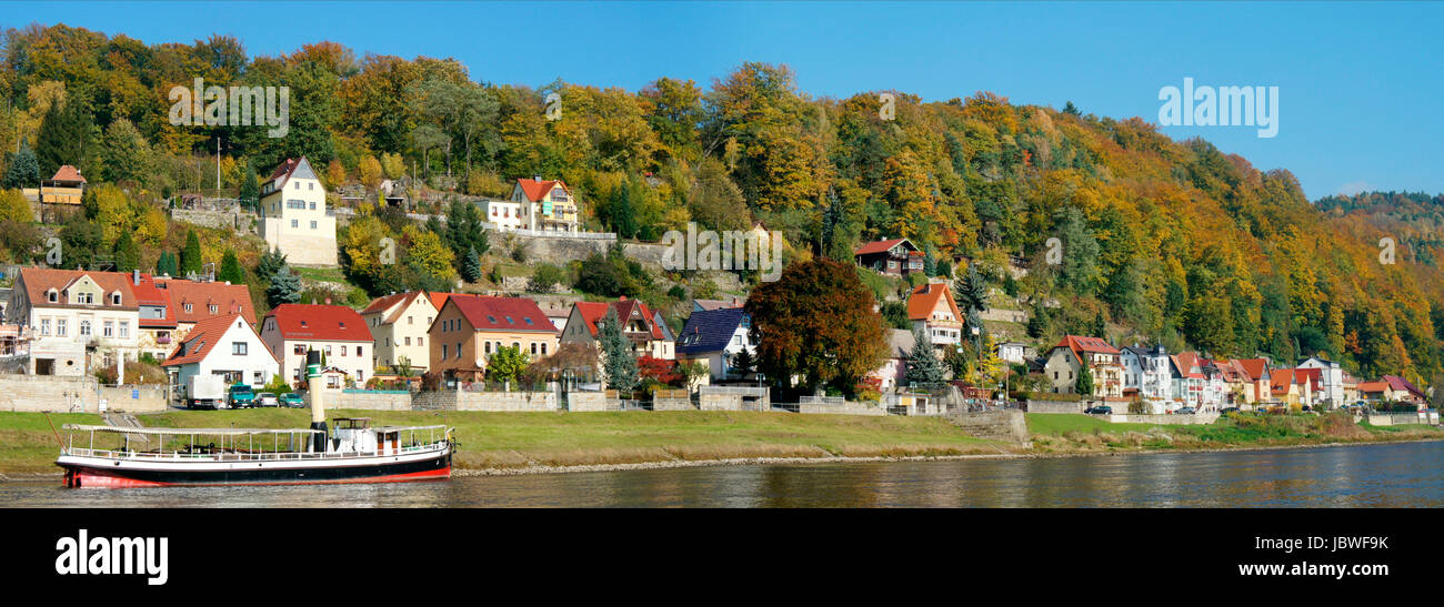 Idyllischer Kurort an der Elbe in der Sächsischen Schweiz in Deutschland, schöne Häuser und bunte Laubwälder, im Vordergrund ein kleiner Dampfer auf der Elbe, panorama idilliaco cittadina termale sull'Elba nella Svizzera sassone in Germania di belle case e coloratissimi boschi di latifoglie, in primo piano di un piccolo sistema di cottura a vapore sul fiume Elba, panorama, Foto Stock